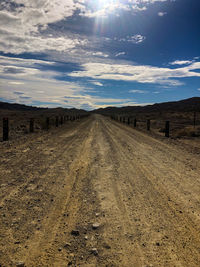 Dirt road amidst land against sky