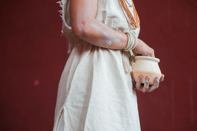 Midsection of woman with pot standing against wall