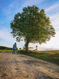 Rear view of man walking on field against sky