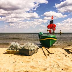 Fishing boat moored at sea shore against cloudy sky