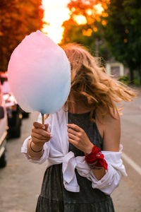 Cute and pretty young girl or student, eats and poses with sugar blue candy cotton on town street