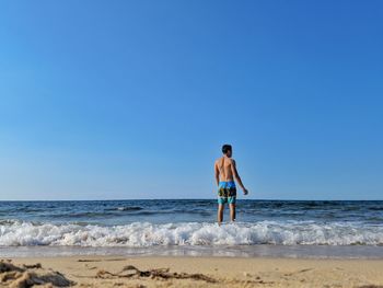 Rear view of shirtless boy on beach against clear sky