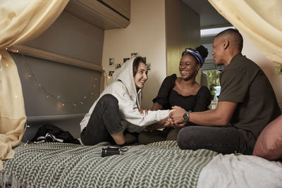 Smiling friends sitting on bed in camper van