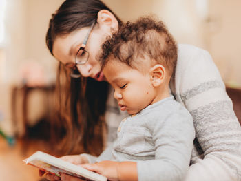 Mother reading book sitting with son at home