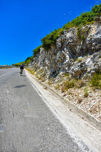 Rear view of man riding bicycle on road against clear blue sky