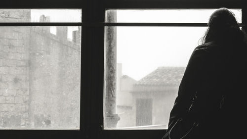 Rear view of woman looking through dusty glass window