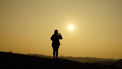 Silhouette woman standing on field against sky during sunset