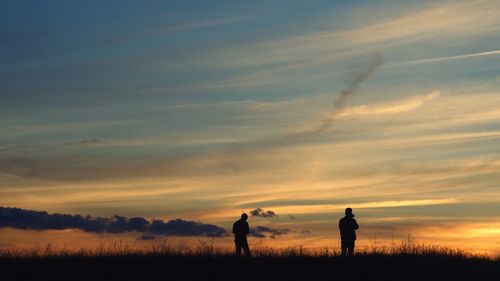 Silhouette people standing on field against sky during sunset