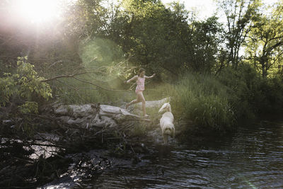 Playful girl with dog running on riverbank during sunny day