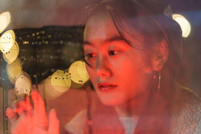 Frustrated korean woman in rainy weather drawing on wet glass unhappy after relationship breakup