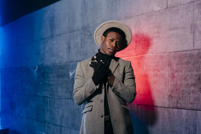 Young man looking away while standing against wall