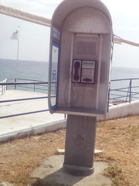 Close-up of telephone booth by sea against sky