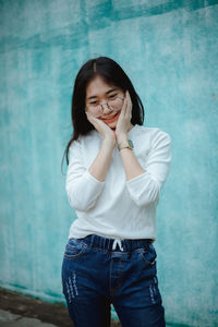 Young woman standing against turquoise wall