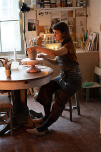 Ceramist in apron molding vase at master class in studio. young woman pottery studio owner at work