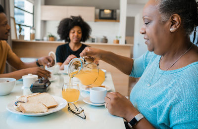 Woman pouring drink in glass while having breakfast with family at home