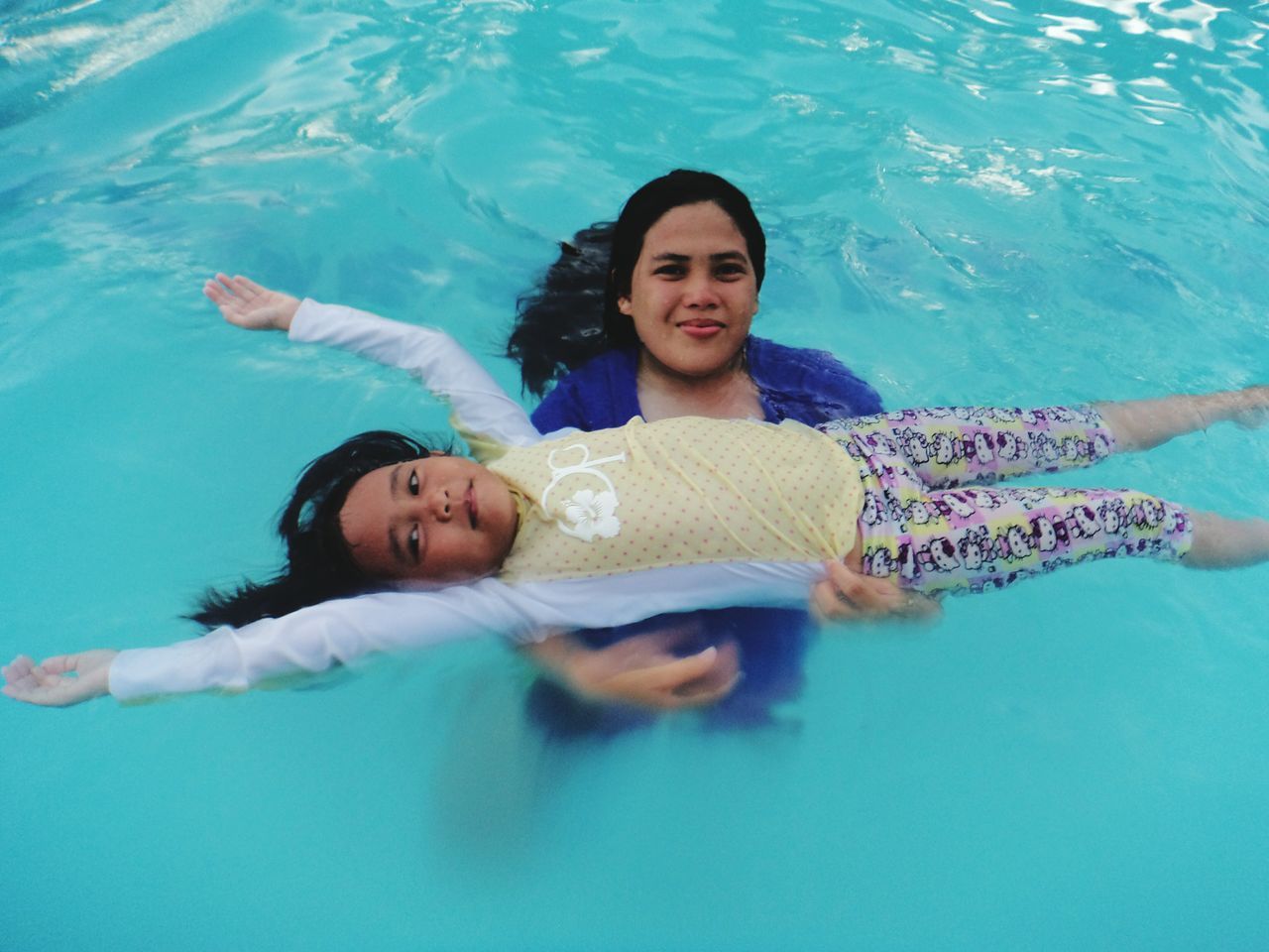 water, swimming pool, child, leisure activity, pool, real people, childhood, women, two people, high angle view, people, togetherness, lifestyles, portrait, swimming, family, looking at camera, motion, front view, outdoors, human arm, positive emotion