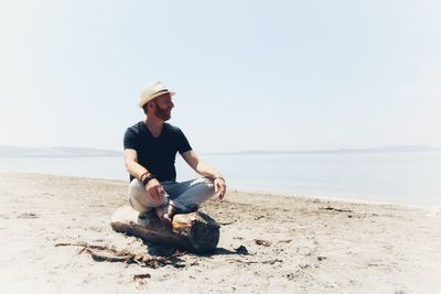 Full length of man sitting on beach against clear sky