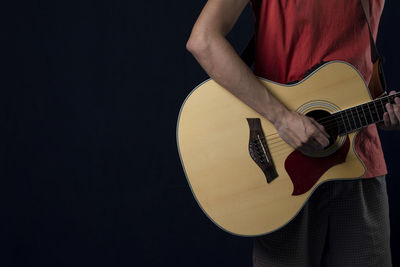 Midsection of man playing guitar against black background