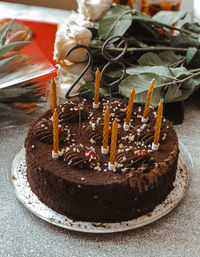 Close-up of chocolate cake on table with number 28 and candles on top and flowers in the background