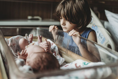 Sister looking at newborn brother in hospital bassinet