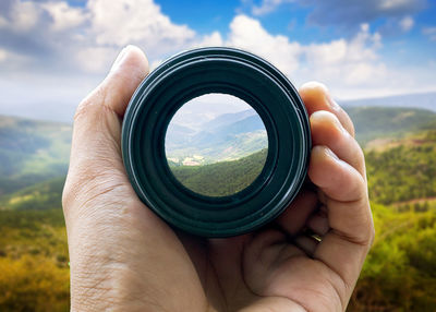 Close-up of hand holding camera against sky