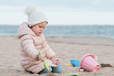 Little girl is digging in the sand on a cold day at the beach