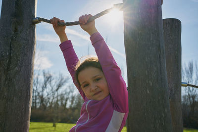 Girl on ropes and zip lines looks into camera with the sun in the background