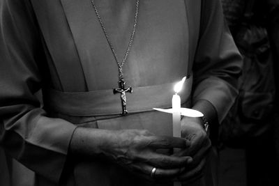 Midsection of nun holding lit candle in dark