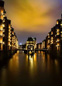 Illuminated buildings by river against sky at night