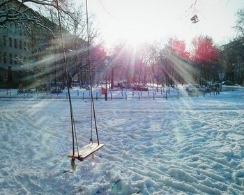 Swing hanging over snow covered field against bright sky