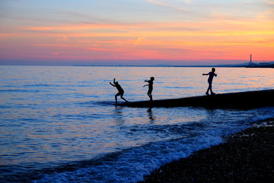 Silhouette children playing on beach during sunset