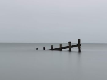 Wooden posts in sea against sky