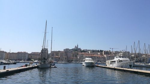 Sailboats moored on canal in city against clear sky