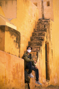 Portrait of man wearing mask sitting on steps outdoors