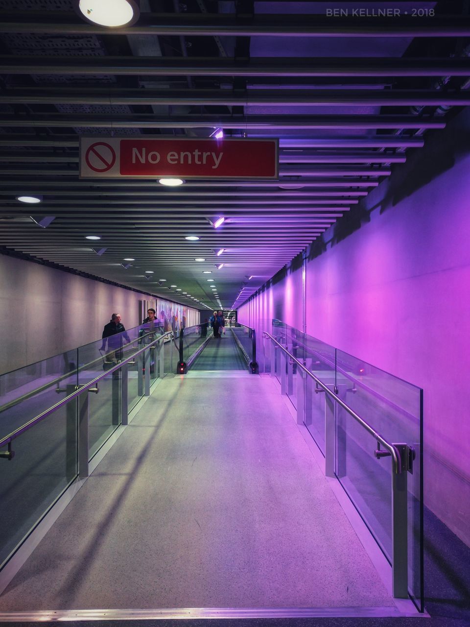 illuminated, architecture, the way forward, direction, lighting equipment, transportation, indoors, built structure, sign, diminishing perspective, incidental people, railing, ceiling, airport, footpath, communication, flooring, light, text, public transportation, modern, moving walkway