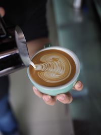 Cropped hand of person pouring milk in cappuccino