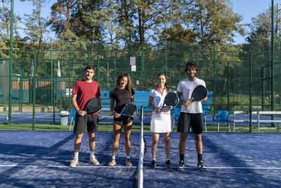 Happy men and women with paddle tennis rackets standing at sports court