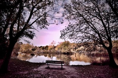 Empty bench by lake against sky during autumn