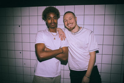 Cheerful young man leaning on friend standing with arms crossed against white background