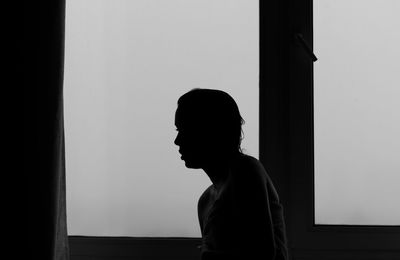 Side view of silhouette woman standing against window at home