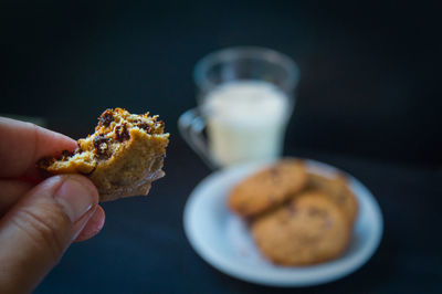Close-up of hand holding a chocolate cookie against black background