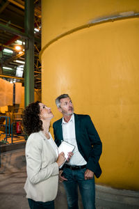 Businesswoman with digital tablet looking up while standing with colleague in industry