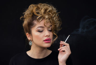 Close-up portrait of young woman smoking over black background