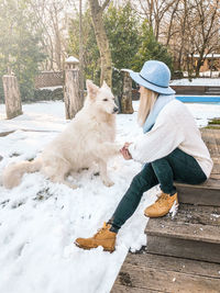 Woman with dog sitting on snowy boardwalk