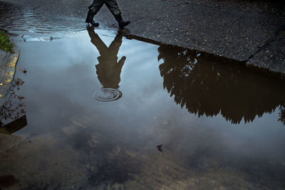 Man walking on road with reflection in puddle
