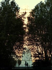 Silhouette people by trees against sky during sunset