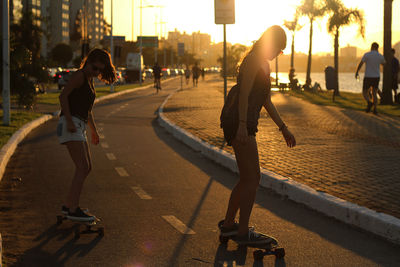 Young women skateboarding on street during sunset