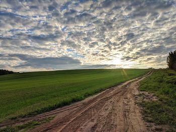 Dirt road amidst field against sky