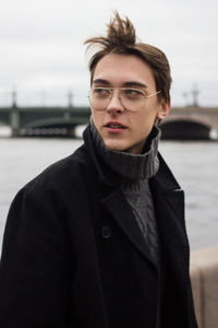 Young man looking away while standing against river and sky