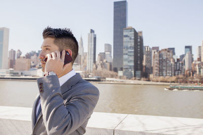 Portrait of a young businessman talking on his smartphone on a rooftop overlooking the city